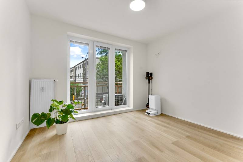 I Na predaj zrekonštruovaný 4i byt v Ružinove, Miletičova - Interiér 4-izbového bytu s podlahou s dreveným dekorom, veľkým oknom a kvetom.