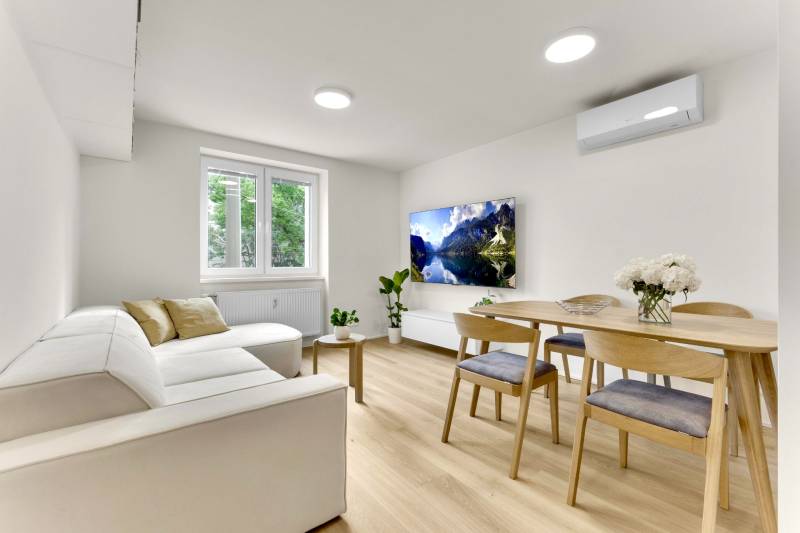 I Na predaj zrekonštruovaný 4i byt v Ružinove, Miletičova - Obývacia izba so sedačkou, jedálenským stolom a podlahou s dreveným dekorom v 4-izbovom byte.