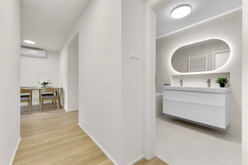 I Na predaj zrekonštruovaný 4i byt v Ružinove, Miletičova - Chodba v 4-izbovom byte s podlahou s dreveným dekorom, pohľad do kúpeľne.