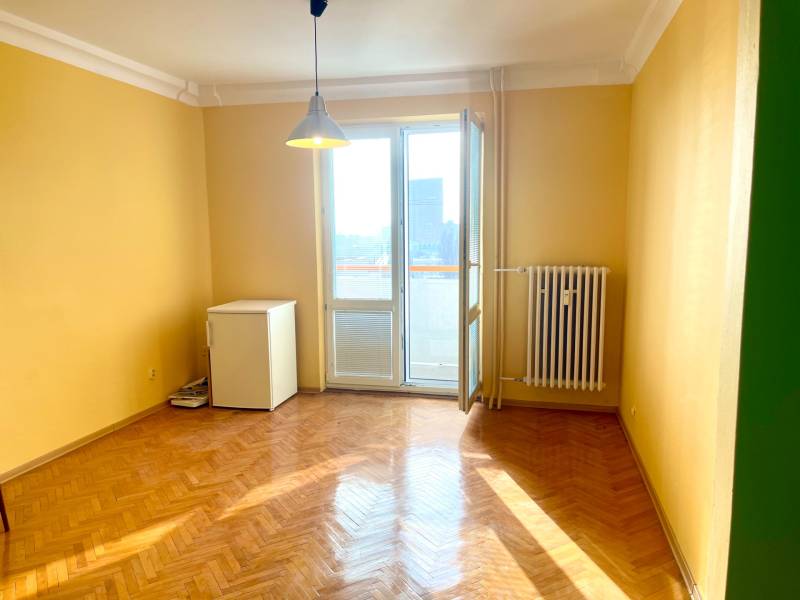 Predáj 1i čiastočne zrekonštruovaný byt s loggiou - Izba s podlahou s dreveným dekorom, žltými stenami a balkónom v 1-izbovom byte.