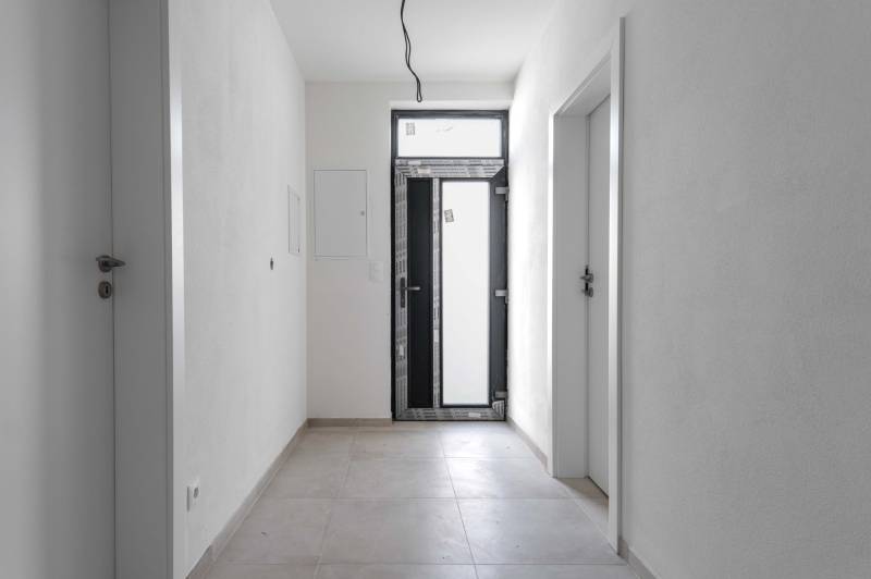 I PREDAJ novostavba 4i rodinného domu s terasou a záhradkou - Vstupná hala v rodinnom dome s bielymi stenami a dlažbou.