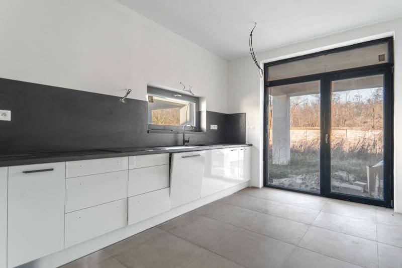 I PREDAJ novostavba 4i rodinného domu s terasou a záhradkou - Kuchyňa v rodinnom dome s bielymi skrinkami, čiernou pracovnou doskou a veľkým oknom.