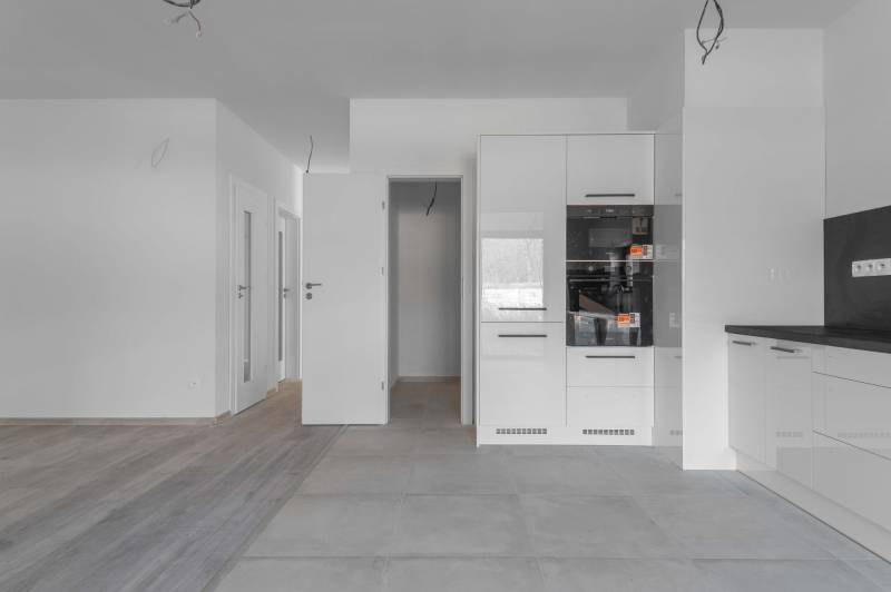 I PREDAJ novostavba 4i rodinného domu s terasou a záhradkou - Kuchyňa v rodinnom dome s bielou kuchynskou linkou a podlahou s dreveným dekorom.