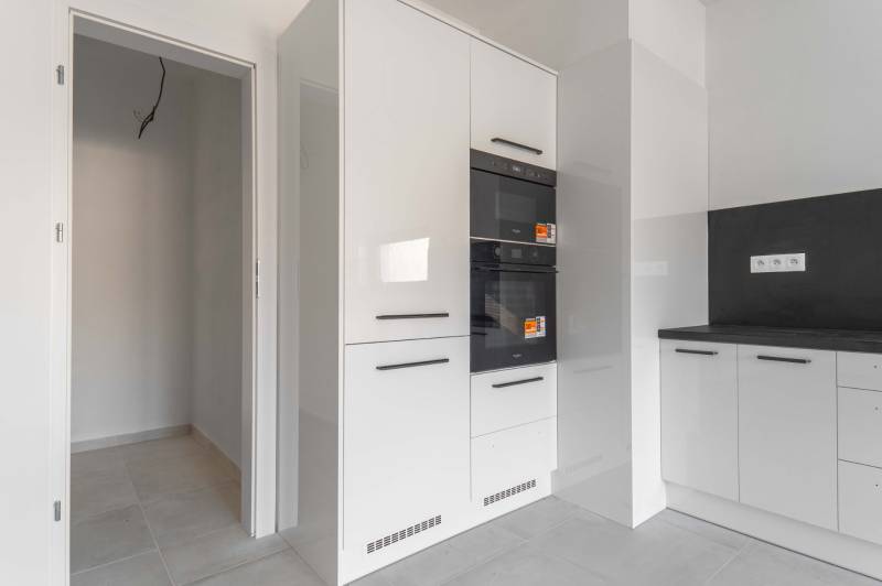 I PREDAJ novostavba 4i rodinného domu s terasou a záhradkou - Kuchynská linka v rodinnom dome s bielymi skriňami a čiernymi úchytkami.