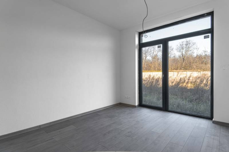 I PREDAJ novostavba 4i rodinného domu s terasou a záhradkou - Izba s veľkým oknom, svetlými stenami a podlahou s dreveným dekorom v rodinnom dome.