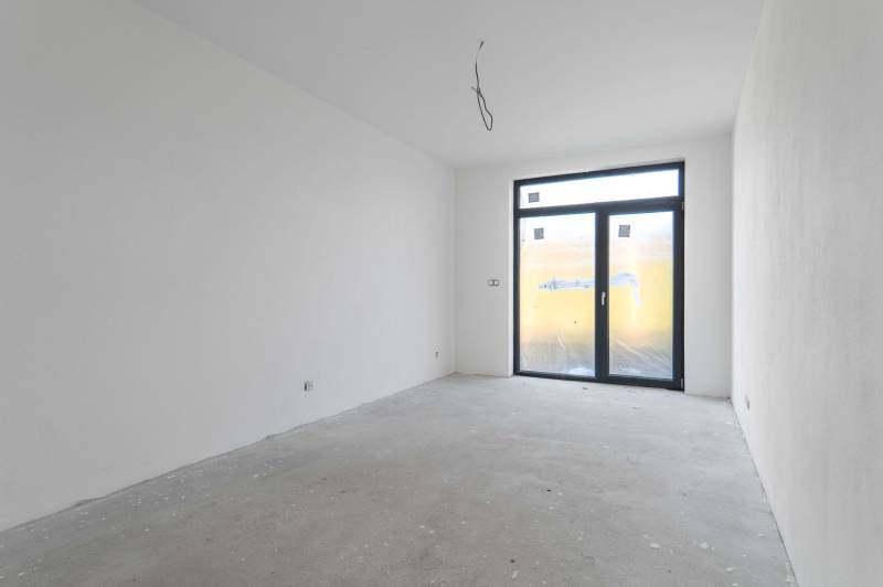 I NA PREDAJ 4i rodinný dom s veľkým pozemkom v Galante - Interiér rodinného domu s bielymi stenami, veľkým oknom a betónovou podlahou.