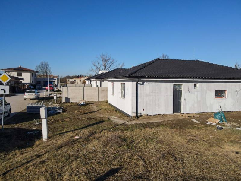 I NA PREDAJ 4i rodinný dom s veľkým pozemkom v Galante - Rodinný dom v Galante s nedokončenou fasádou, okolitým terénom a autami na ulici.