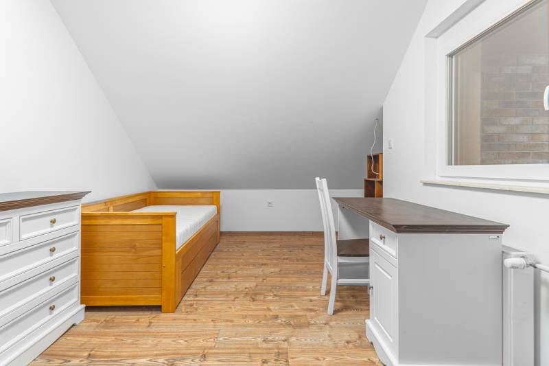 I Predaj štýlového tehlového domu v Rajke pri Bratislave - Podkrovná izba s posteľou, písacím stolom a podlahou s dreveným dekorom v rodinnom dome.