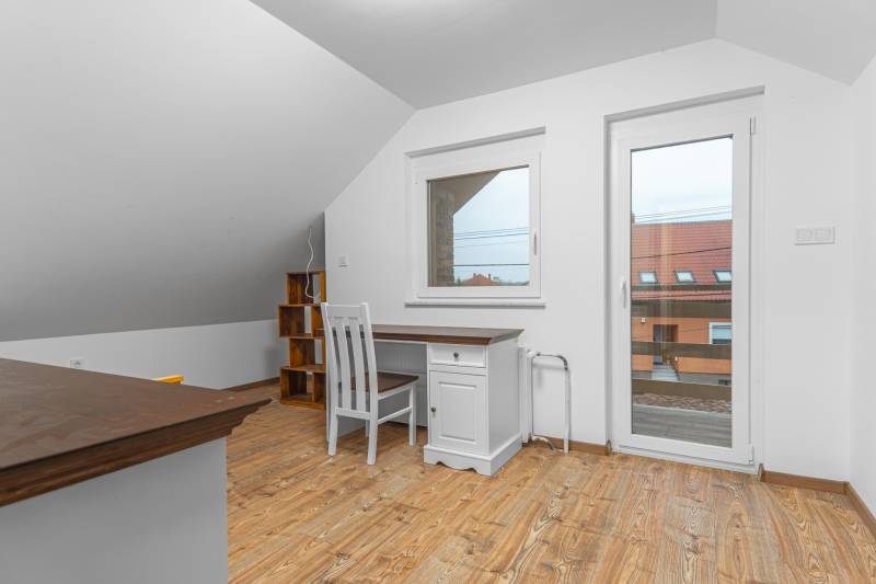 I Predaj štýlového tehlového domu v Rajke pri Bratislave - Interiér rodinného domu s podlahou s dreveným dekorom, písací stôl a stolička.