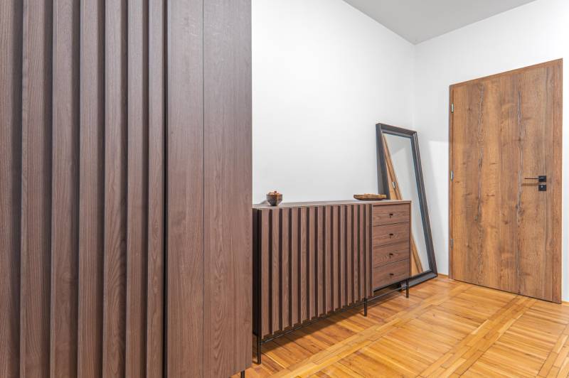 I Predaj štýlového tehlového domu v Rajke pri Bratislave - Interiér rodinného domu s komodou, zrkadlom a podlahou s dreveným dekorom.