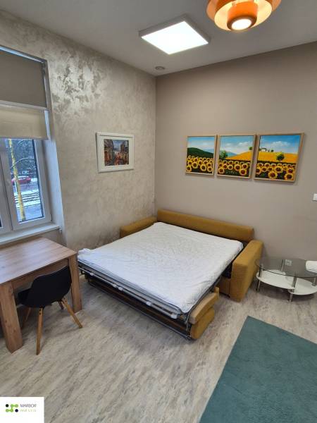 Na prenájom  plne zariadený apartmán na Južnej triede 44, Košice - Izba s rozkladacou pohovkou, stolom a kreslom, podlaha s dreveným dekorom.