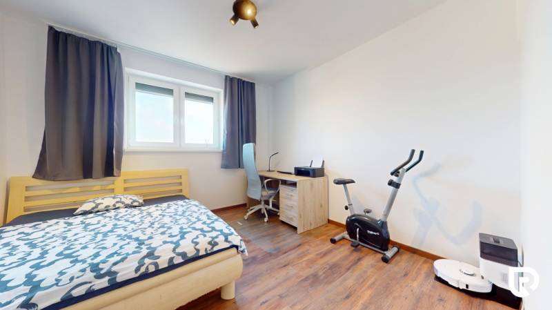 | Exkluzívny 4-izbový byt s obrovskou terasou | Stupava - Izba v 4-izbovom byte s posteľou, pracovným stolom, rotopedom a podlahou s dreveným dekorom.