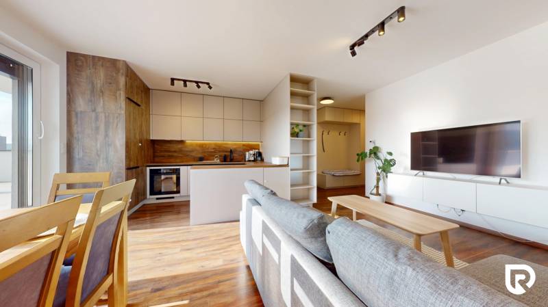 | Exkluzívny 4-izbový byt s obrovskou terasou | Stupava - Interiér 4-izbového bytu s kuchyňou, pohovkou a podlahou s dreveným dekorom.