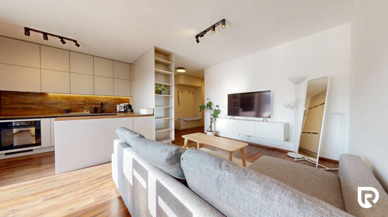 | Exkluzívny 4-izbový byt s obrovskou terasou | Stupava - Obývačka so svetlou pohovkou, kuchyňou a podlahou s dreveným dekorom v 4-izbovom byte.