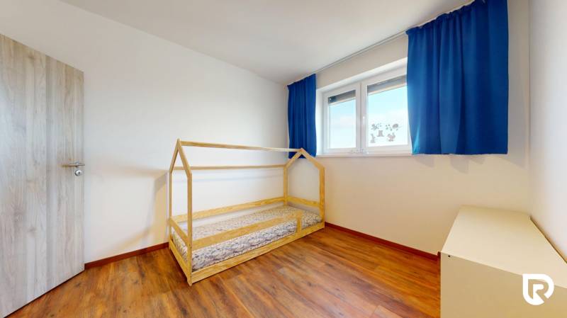 | Exkluzívny 4-izbový byt s obrovskou terasou | Stupava - Detská izba v 4-izbovom byte s podlahou s dreveným dekorom a modrými závesmi.