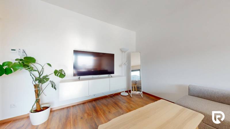 | Exkluzívny 4-izbový byt s obrovskou terasou | Stupava - Obývačka 4-izbového bytu s televízorom, kvetinou a podlahou s dreveným dekorom.