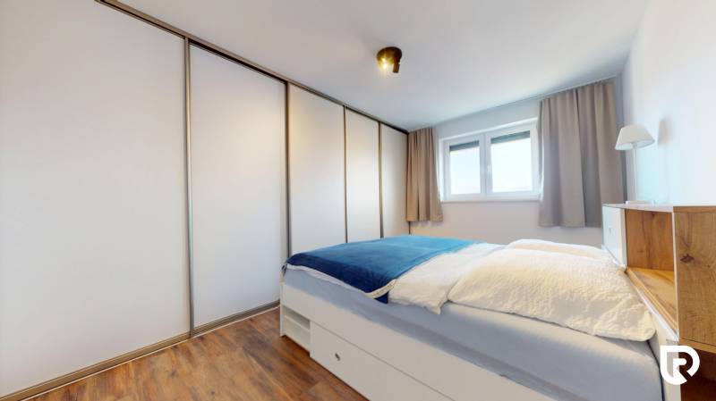 | Exkluzívny 4-izbový byt s obrovskou terasou | Stupava - Spálňa v 4-izbovom byte s posteľou, vstavanou skriňou a podlahou s dreveným dekorom.