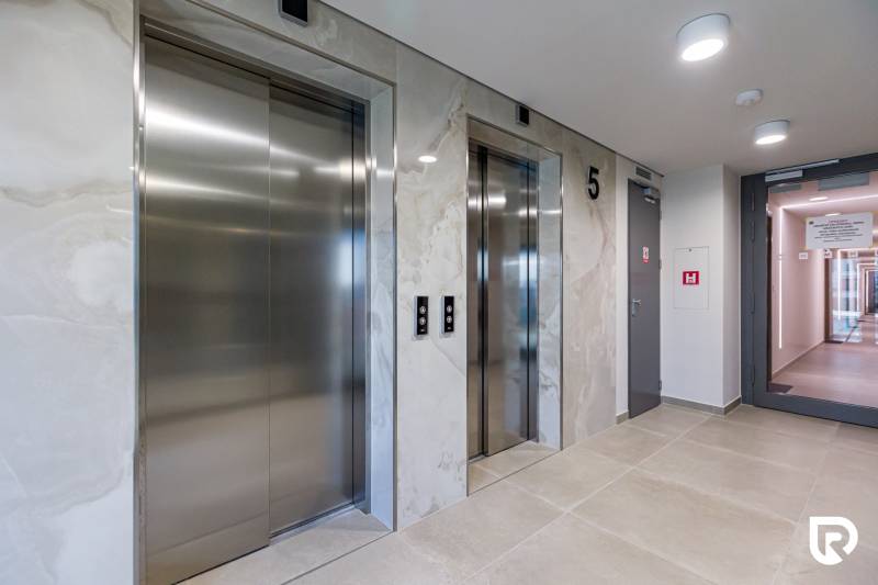 REZERVOVANÉ I METROPOLIS I Luxusný 1i byt I Staré Mesto - Chodba s dvoma výťahmi a modernými obkladmi v bytovom dome.
