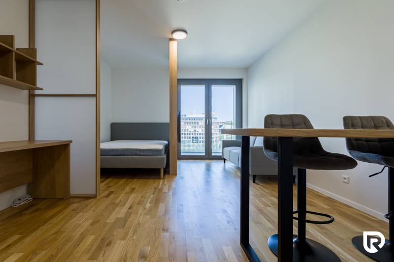 REZERVOVANÉ I METROPOLIS I Luxusný 1i byt I Staré Mesto - Interiér 1-izbového bytu s podlahou s dreveným dekorom, posteľou a pracovným stolom.