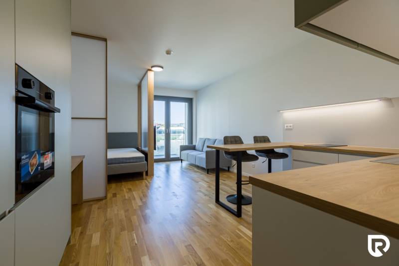 REZERVOVANÉ I METROPOLIS I Luxusný 1i byt I Staré Mesto - Interiér 1-izbového bytu s podlahou s dreveným dekorom, kuchynským ostrovčekom a sedačkou.