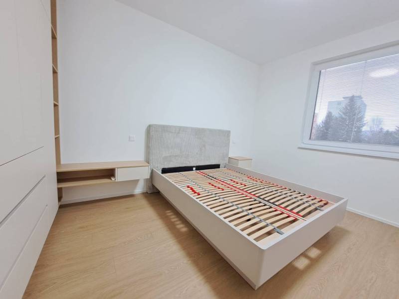 Prenájom: Lukratívny 2-izbový byt v Poprade na Novom nábreží - Spálňa v 2-izbovom byte s podlahou s dreveným dekorom, veľké okno, posteľ a úložný priestor.