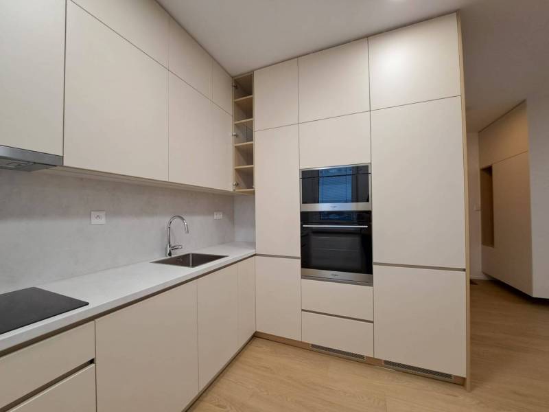 Prenájom: Lukratívny 2-izbový byt v Poprade na Novom nábreží - Kuchyňa v 2-izbovom byte s podlahou s dreveným dekorom, svetlými skrinkami a vstavanou rúrou.