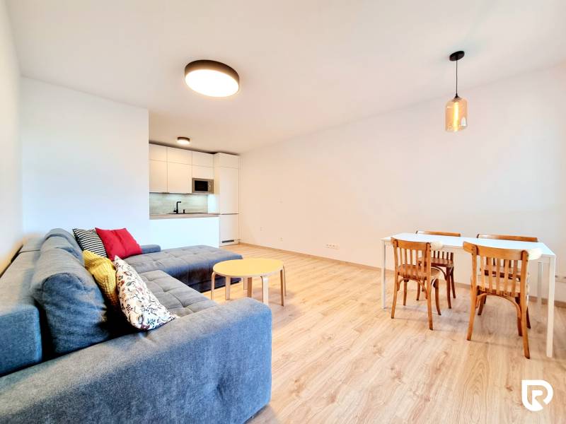 Pekný a moderný 3-izbový byt I Arboria Trnava - Obývacia izba v 3-izbovom byte s kuchynským kútom a podlahou s dreveným dekorom.