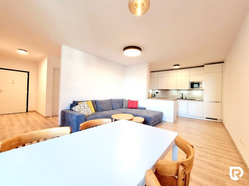 Pekný a moderný 3-izbový byt I Arboria Trnava - Obývačka v 3-izbovom byte s podlahou s dreveným dekorom, pohodlnou sedačkou a kuchynským kútom.