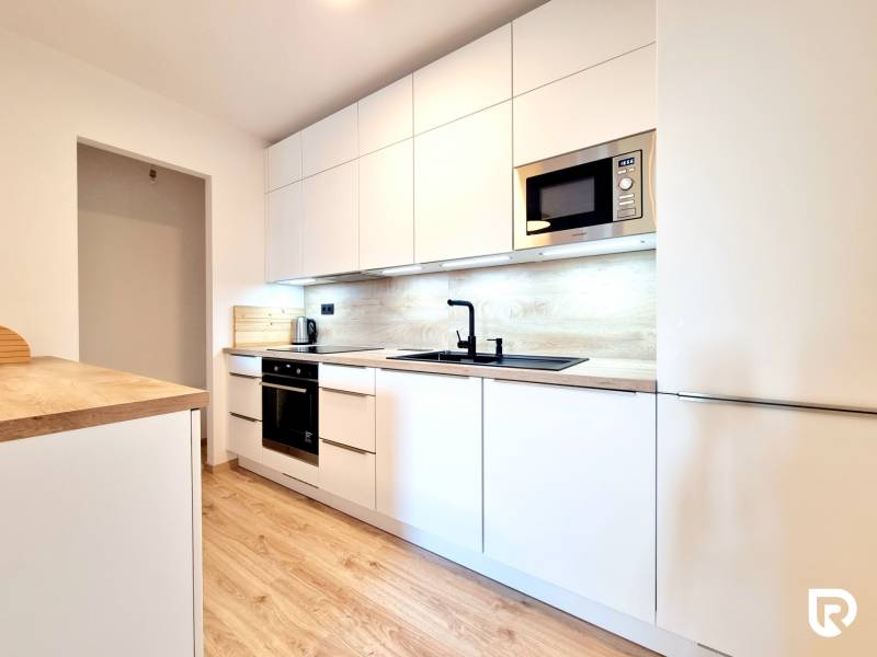 Pekný a moderný 3-izbový byt I Arboria Trnava - Kuchyňa v 3-izbovom byte s bielymi skrinkami a podlahou s dreveným dekorom.