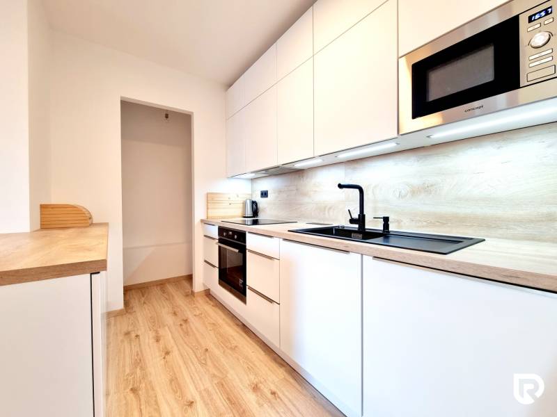 Pekný a moderný 3-izbový byt I Arboria Trnava - Kuchyňa s bielymi skrinkami a podlahou s dreveným dekorom v 3-izbovom byte.