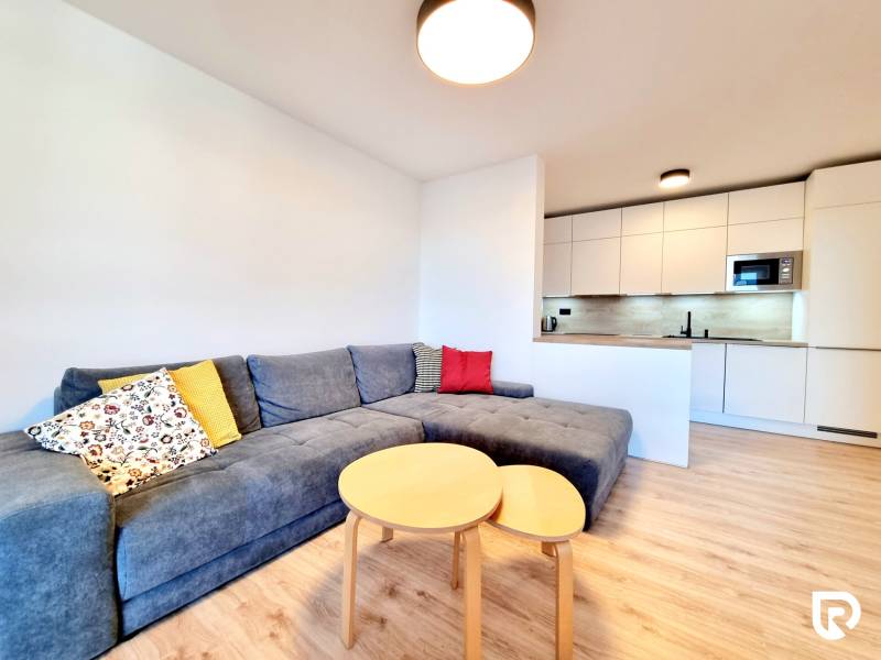 Pekný a moderný 3-izbový byt I Arboria Trnava - Obývací priestor v 3-izbovom byte so sivou sedačkou a kuchyňou, podlaha s dreveným dekorom.