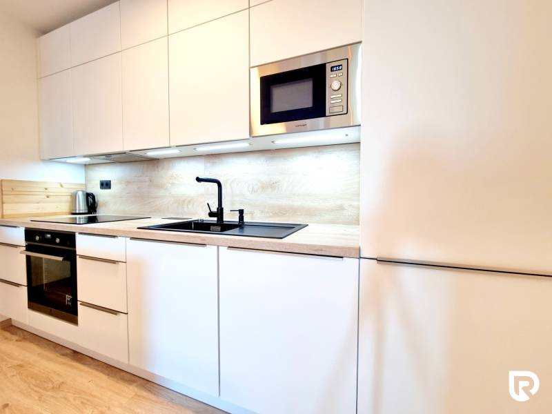 Pekný a moderný 3-izbový byt I Arboria Trnava - Kuchyňa v 3-izbovom byte s bielymi skrinkami a podlahou s dreveným dekorom.