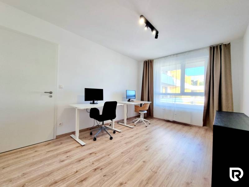 Pekný a moderný 3-izbový byt I Arboria Trnava - Pracovňa v 3-izbovom byte s dvomi stolmi, podlaha s dreveným dekorom, veľké okno.