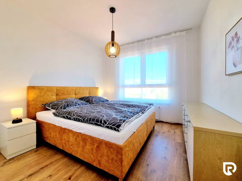 Posledný investičný krásny 2-izbový byt | 55 m² | RÍNOK RAČA - Spálňa s pohodlnou posteľou, lampou a komodou v 2-izbovom byte, podlaha s dreveným dekorom.