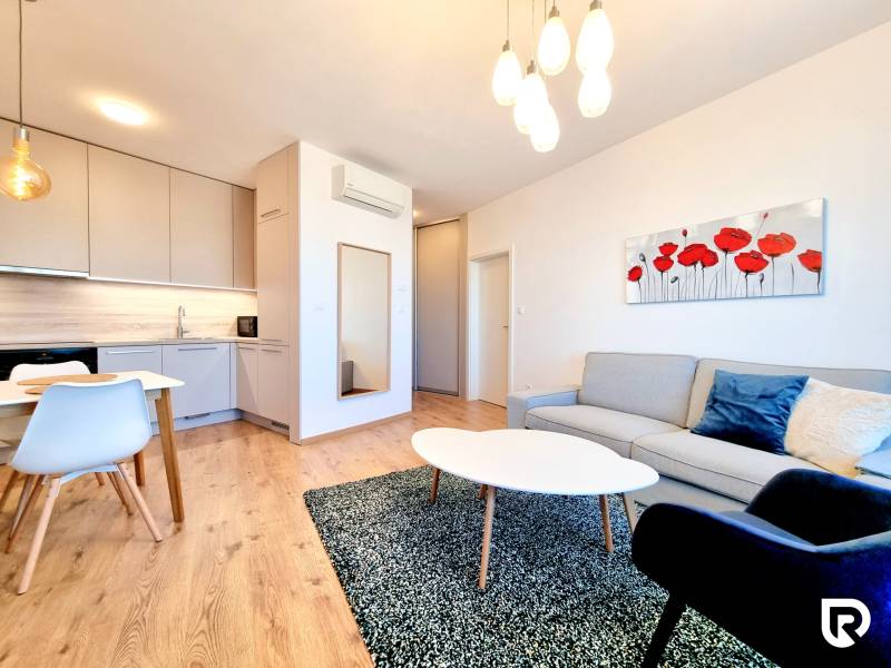 Posledný investičný krásny 2-izbový byt | 55 m² | RÍNOK RAČA - Svetlá obývačka s podlahou s dreveným dekorom, pohodlným sedením a elegantným umením na stene.