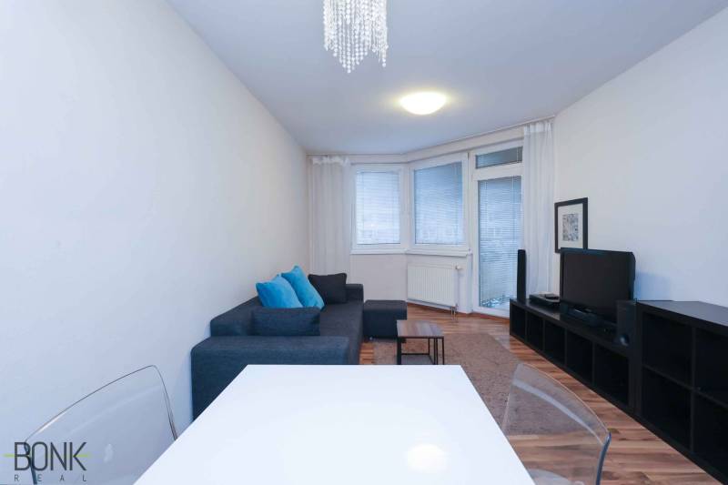 Predaj útulný 2 izbový byt, novostavba, super lokalita Jégeho ulica. - Obývačka 2-izbového bytu s gaučom, televízorom a podlahou s dreveným dekorom.