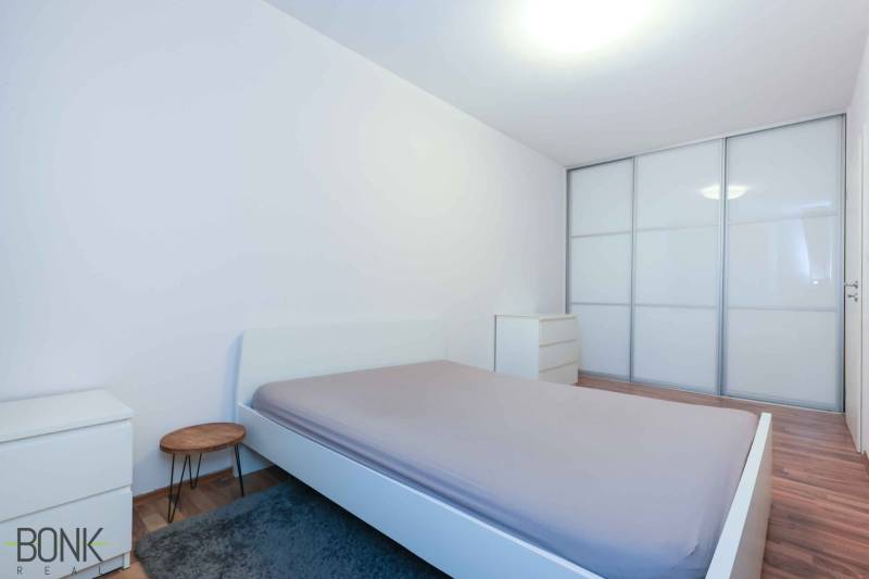 Predaj útulný 2 izbový byt, novostavba, super lokalita Jégeho ulica. - Spálňa v 2-izbovom byte s veľkou vstavanou skriňou a podlahou s dreveným dekorom.