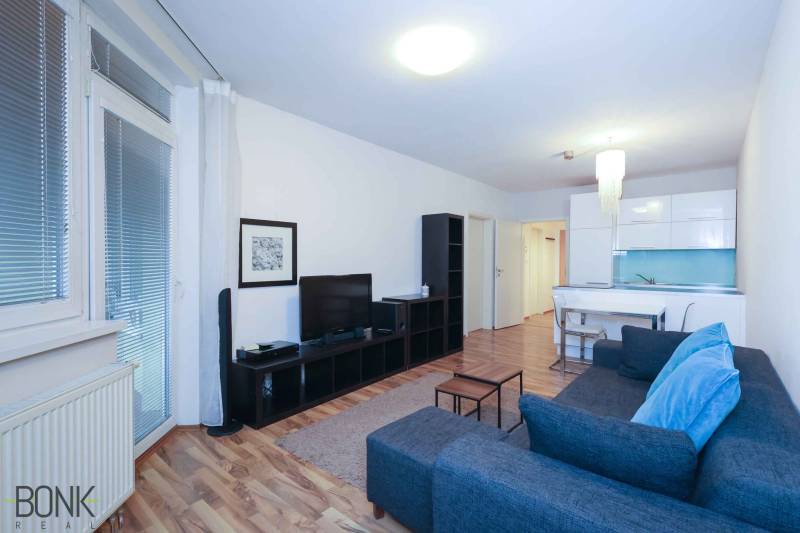 Predaj útulný 2 izbový byt, novostavba, super lokalita Jégeho ulica. - Obývacia izba 2-izbového bytu s podlahou s dreveným dekorom a štýlovým nábytkom.