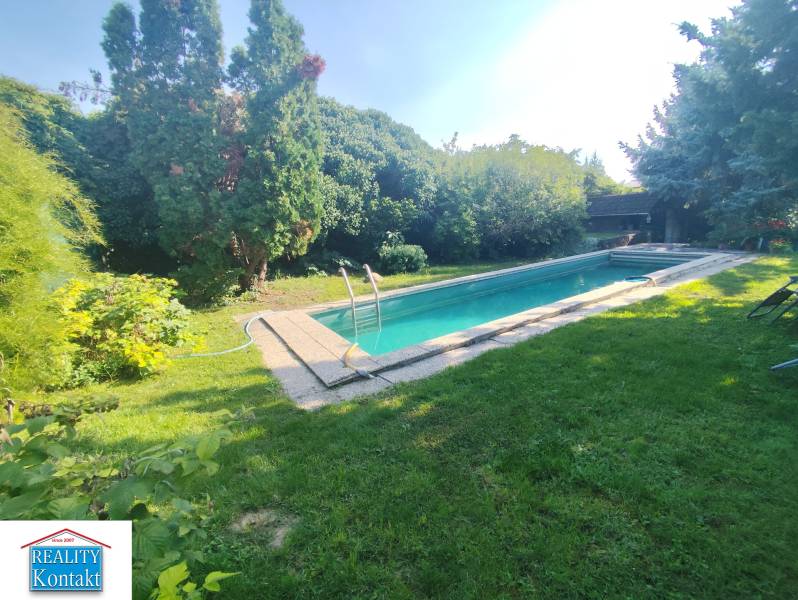 Ponúkame na predaj záhradný domček - Jasová - Záhrada rodinného domu v Jasovej s bazénom obklopená zeleňou a stromami.