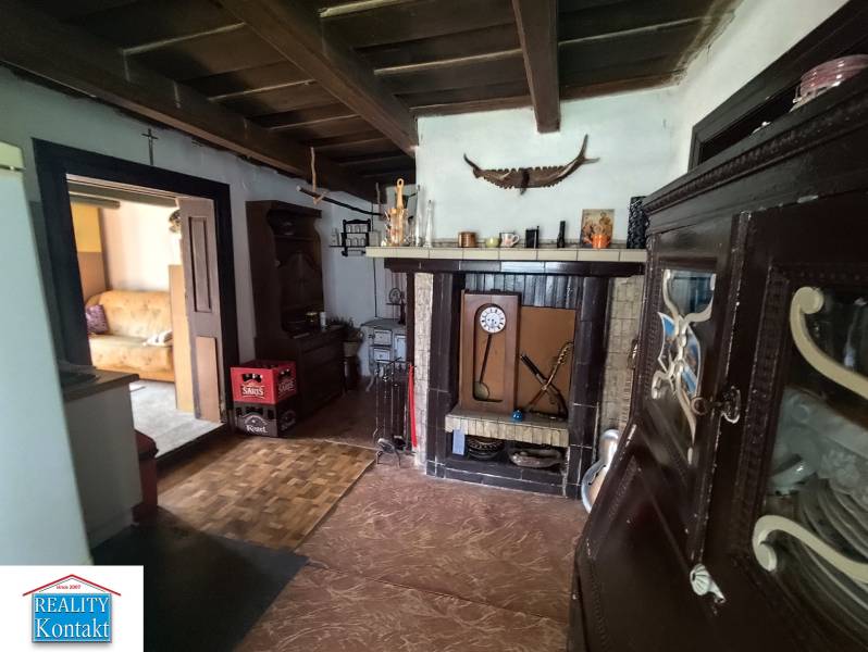 Ponúkame na predaj záhradný domček - Jasová - Interiér rodinného domu s kozubom, dekoratívnym riadom a otvorenými dverami do obývacej izby.