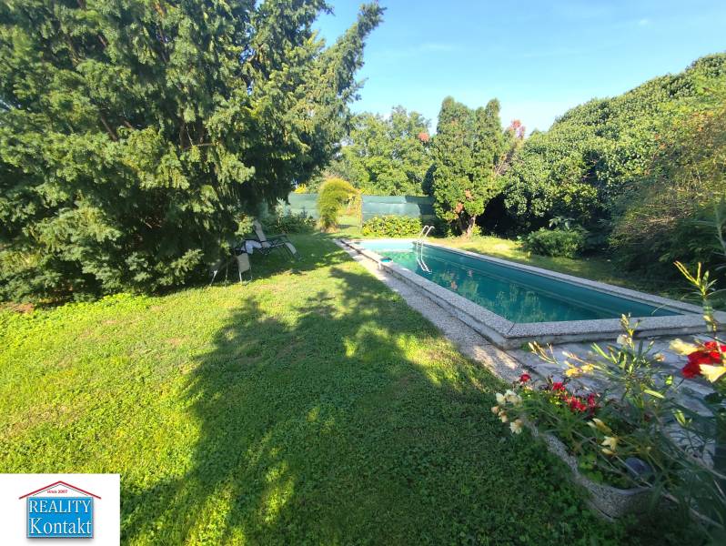 Ponúkame na predaj záhradný domček - Jasová - Záhrada rodinného domu v Jasovej s bazénom obklopená zeleňou a stoličkami.