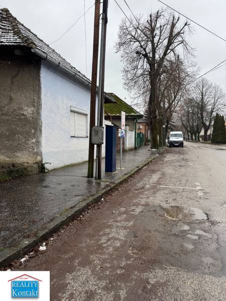 Predáme rodinný dom- Šurany, širšie centrum.  - Rodinný dom na Komenského ulici v Šuranoch, pri ceste s elektrickým stĺpom a stromami.