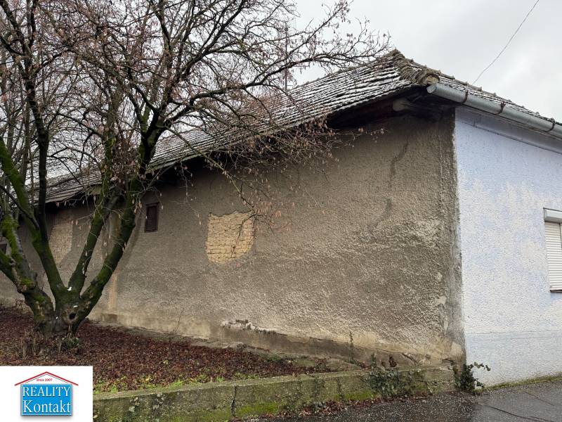Predáme rodinný dom- Šurany, širšie centrum.  - Rodinný dom na Komenského ulici v Šuranoch s viditeľným holým múrom a stromom.