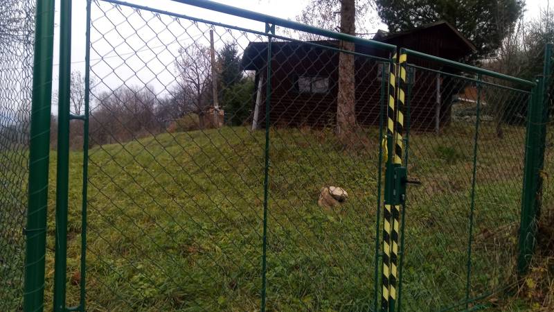 KONSKÉ - pozemok 1108 m2,okr. Martin  - Brána so zeleným pletivom, vedúca na trávnatý pozemok, blízko drevené obydlie.