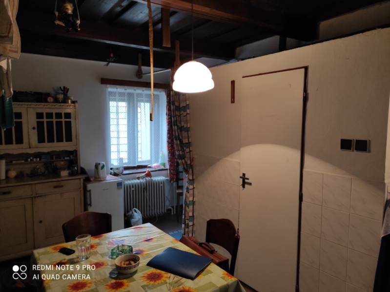 ČREMOŠNÉ-chalupa na pozemku 700m2   - Kuchyňa v rodinnom dome s dreveným stropom, stolom a jednoduchým nábytkom.