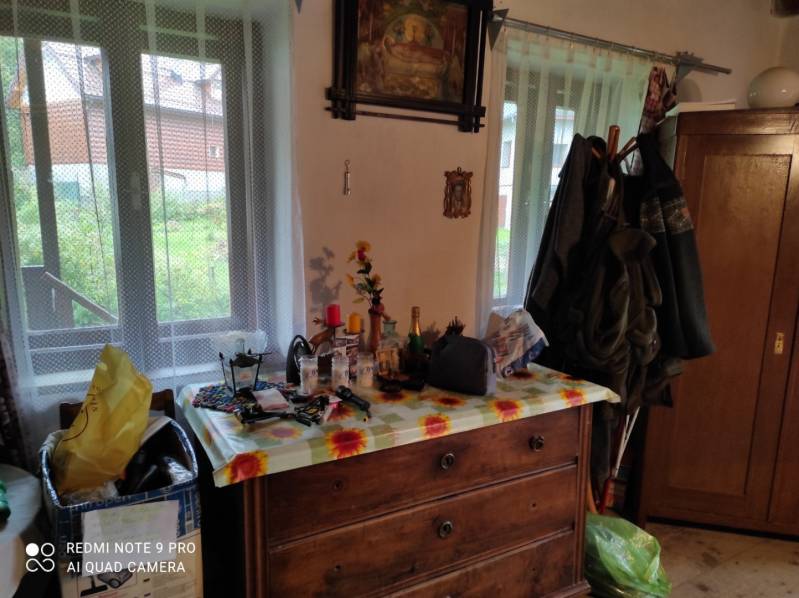 ČREMOŠNÉ-chalupa na pozemku 700m2   - Drevená komoda v rodinnom dome obklopená predmetmi, obrazy, zavesená bunda.