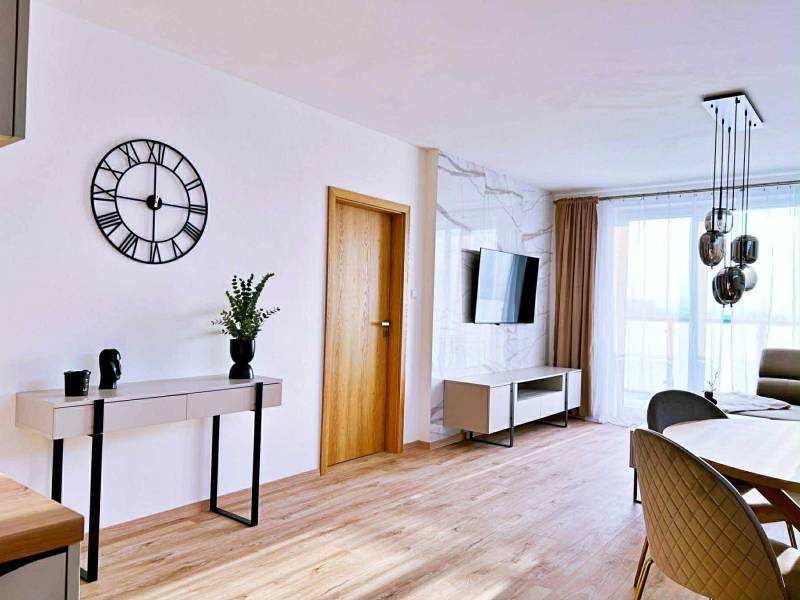 NADŠTANDARDNÝ 3-IZBOVÝ BYT NA PRENÁJOM | Byty Solivarská, Prešov - Obývacia izba v 3-izbovom byte s podlahou s dreveným dekorom, stolom a televízorom.