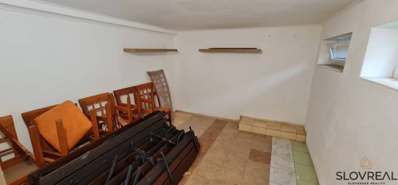 Predaj Domu v obci Lovča - Prázdna miestnosť s policami, stoličkami a dvoma malými oknami v rodinnom dome.