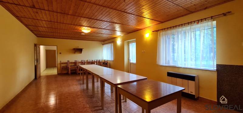 Predaj Domu v obci Lovča - Jedáleň v rodinnom dome s drevenými stropmi, dlhými stolmi a stoličkami, svetlá výzdoba.