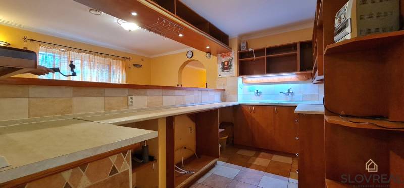 Predaj Domu v obci Lovča - Kuchyňa v rodinnom dome s drevenými skrinkami, osvetlením a dlažbou.